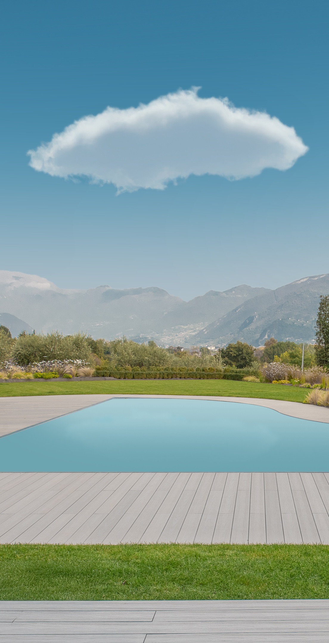 Una piscina in un giardino davanti alle montagne, con una nuvola che la sovrasta